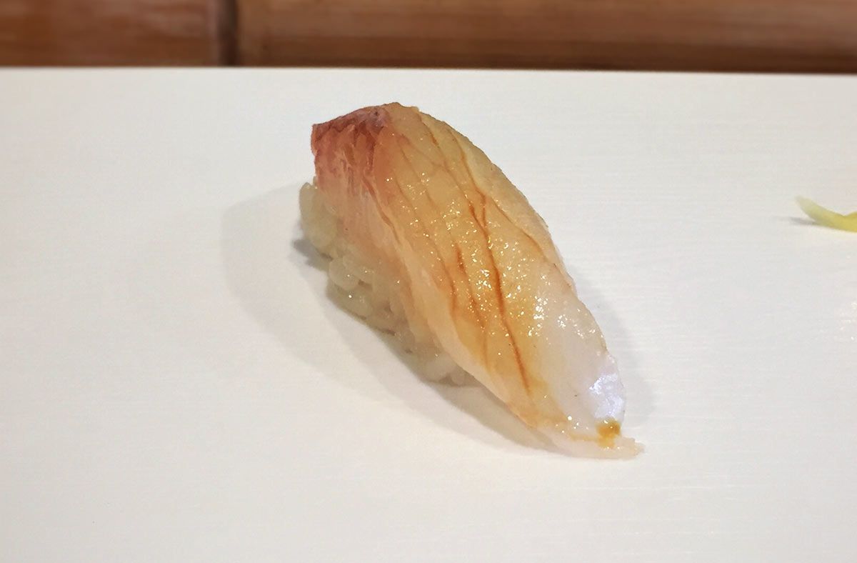 A single Nigiri sushi with a glossy, delicate fish topping on a plate