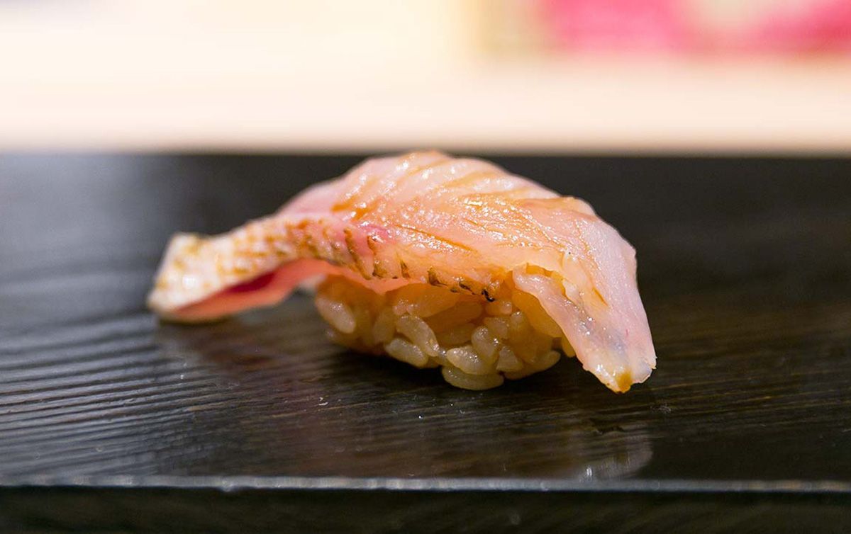 Carefully crafted Akamutsu Nigiri Sushi on a glossy black plate, lightly seasoned with soy sauce for the perfect flavor.