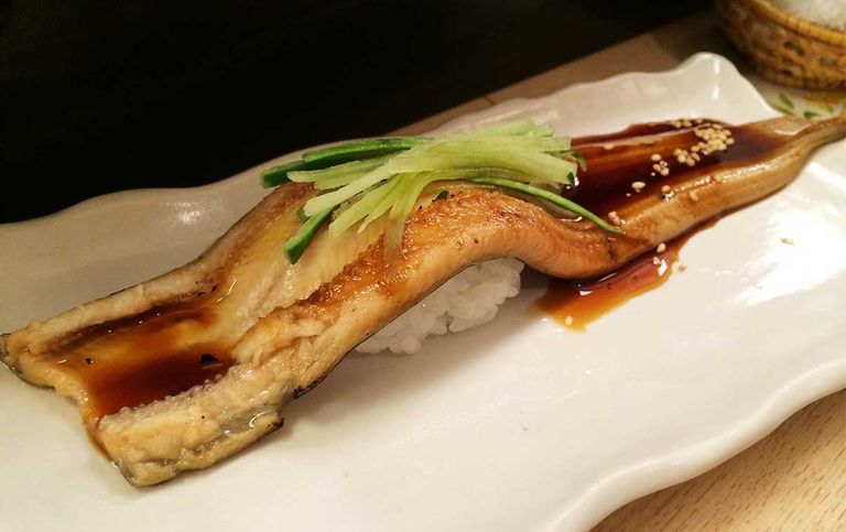 Eel nigiri sushi drizzled with nitsume sauce and garnished with cucumber strips, on a white plate