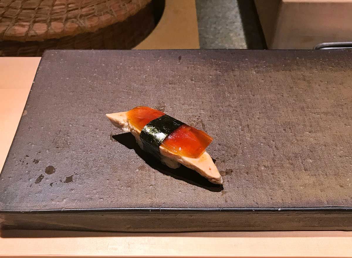 Ein Stück Nigiri Sushi mit Fischleber, belegt mit eingelegter Wassermelone, präsentiert auf einem Steinplattenteller