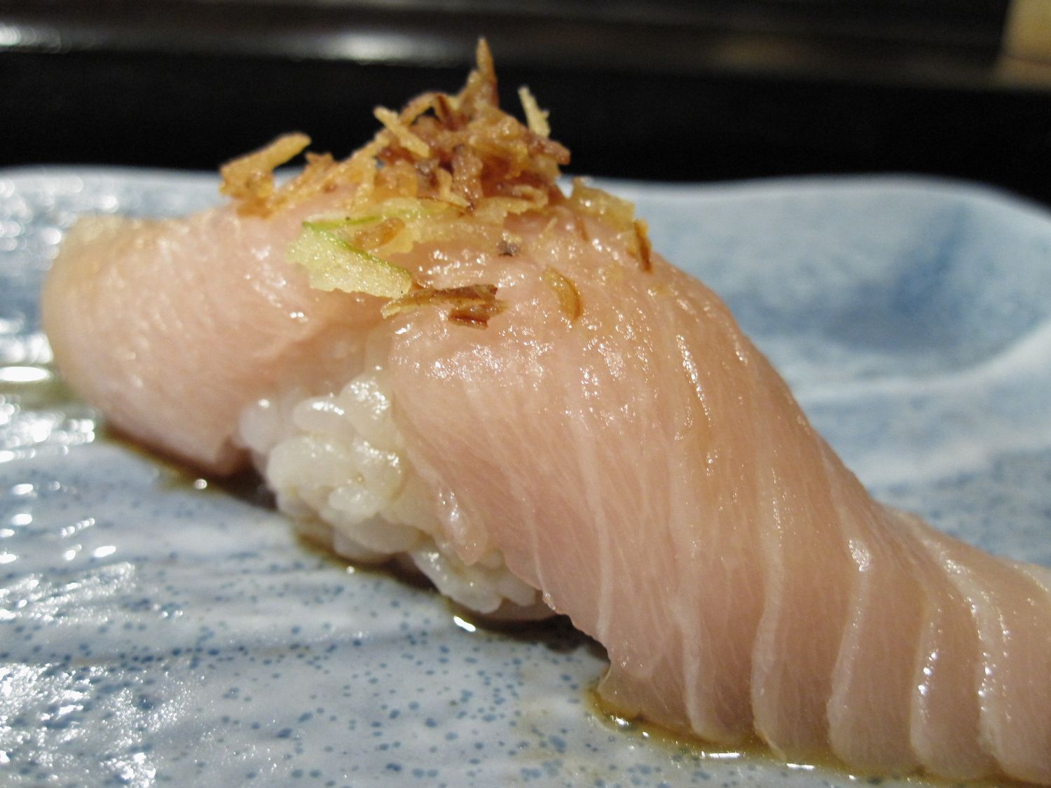 Nigiri sushi with albacore belly meat topped with fried onions, presented on a blue ceramic plate.