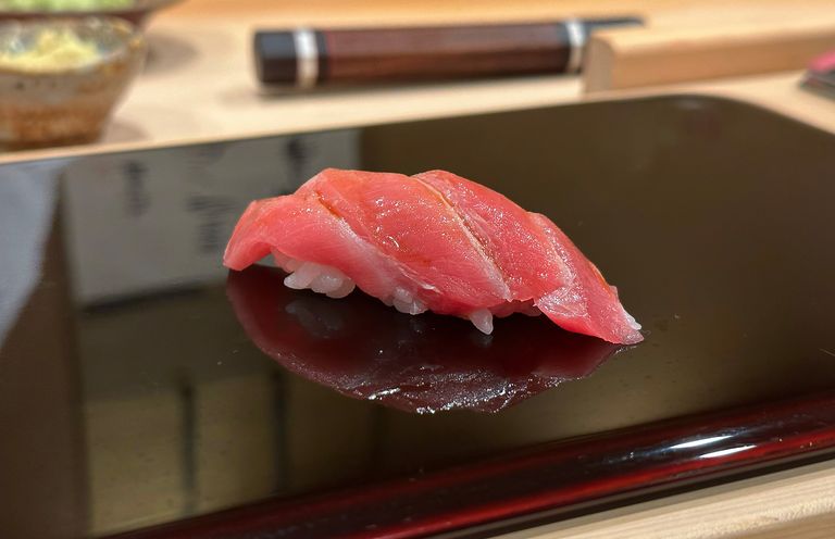 At the bar of a sushi restaurant, a freshly prepared piece of nigiri sushi with fatty tuna (otoro in Japanese) lies on a serving tray.