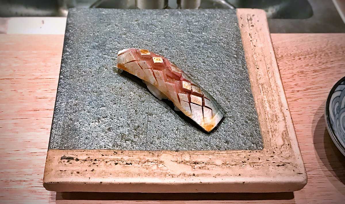 Iwashi sushi, a sardine nigiri, artfully served on a stone plate.