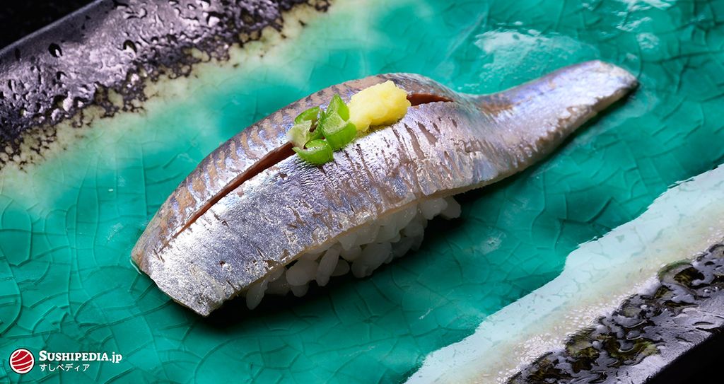 Detailed view of sardine sushi nigiri with pickled ginger and wasabi on a turquoise ceramic plate
