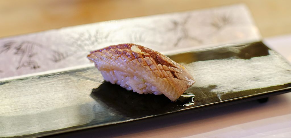 Close-up of iwashi sushi nigiri on a rectangular plate with Japanese decor