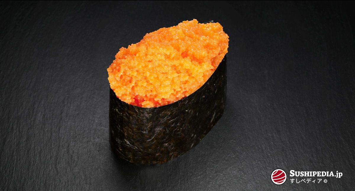 A Gunkan sushi topped with bright orange Masago (capelin roe) wrapped in a seaweed sheet, presented on a dark background.