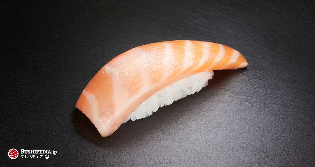 A piece of salmon belly sushi nigiri, placed on a dark background. The pronounced grain of the belly fat is clearly visible.
