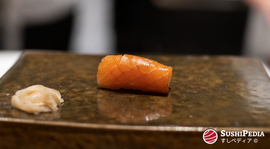 A piece of salmon sushi (samon or sake sushi), garnished with konbu, lies on a traditional ceramic plate.