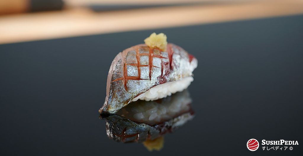 Ein einzelnes, frisch zubereitetes Stück Aji Sushi, liegt auf einer glänzenden Platte in einem Restaurant.