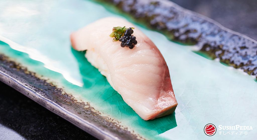 A hand-formed sushi (Japanese nigiri) with Japanese amberjack or yellowtail (Japanese hamachi) lies on a Japanese ceramic plate. It is garnished with a topping of marinated shiso and caviar roe.