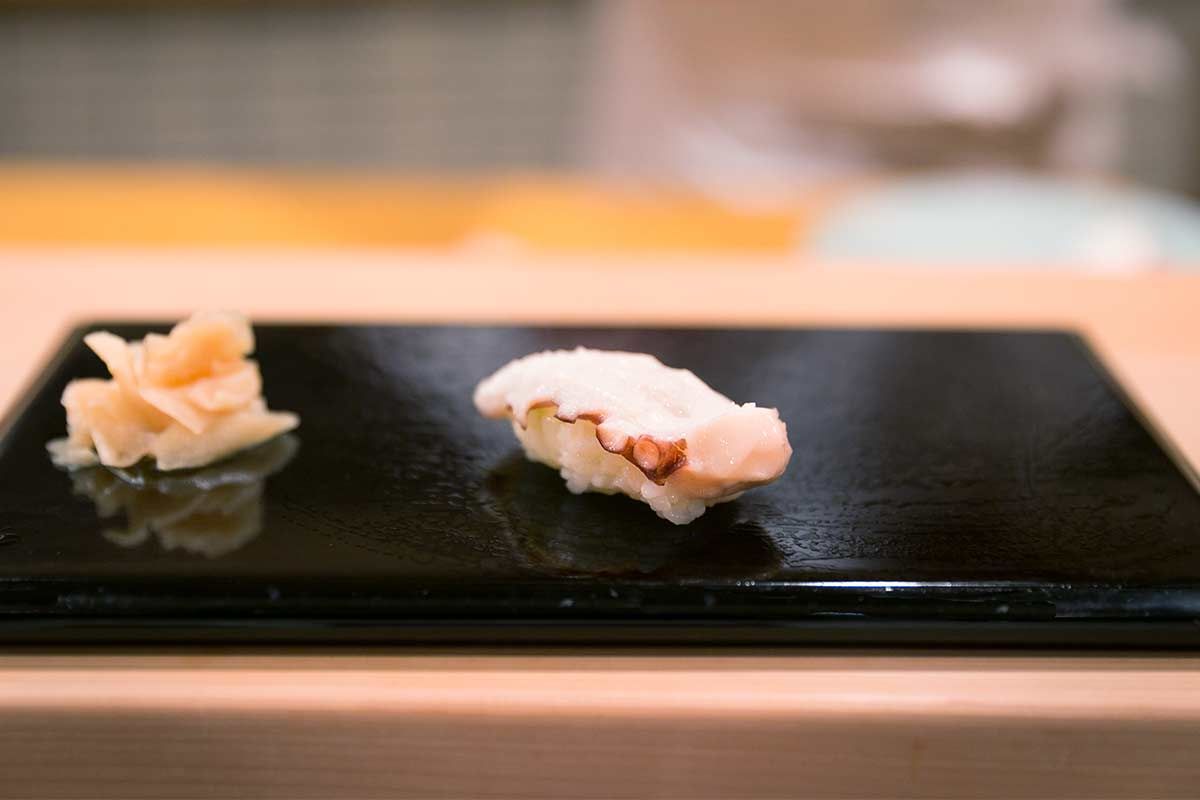 A piece of Tako Sushi next to pickled ginger on a black ceramic plate