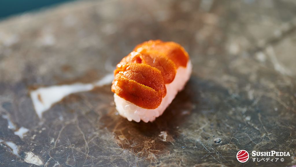 A piece of Uni Nigiri Sushi, with sea urchin roe (uni) placed on a small portion of sushi rice, served on a dark marble surface.