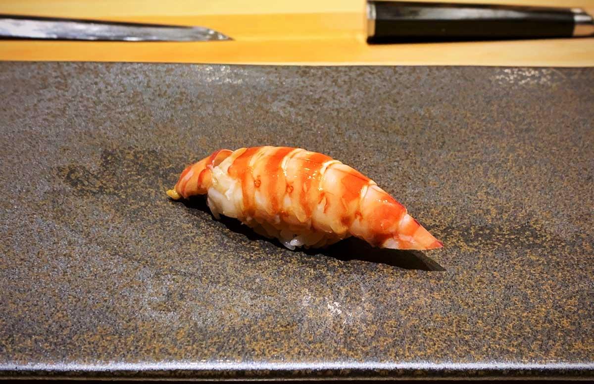 Kuruma ebi nigiri sushi on a dark plate. 
				T.Tseng. 
				Kuruma ebi. 
				flickr.com. 
				Attribution 2.0 Generic (CC BY 2.0). 
				