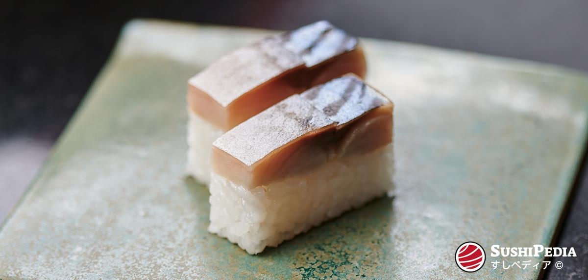 Pressed mackerel (saba) sushi placed on a glazed clay slab.